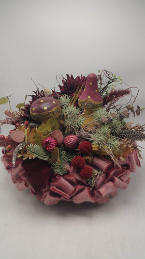 Herbstgesteck in Bordeaux mit zwei Holzpilzen, dunkelroten Chrysanthemen und Tannenzweigen auf rosa Filzkranz