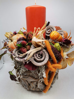Herbstgesteck mit orangefarbener Stumpenkerze, Kürbissen, Ziermais und Beeren in Rindentopf, Ansicht von vorn