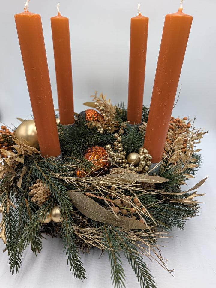 Adventskranz mit vier orangefarbenen Stabkerzen, Tannenzweigen, goldenen Kugeln, Zapfen und goldenen Beerenzweigen