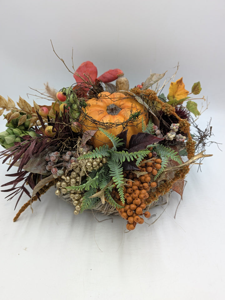 Flaches Herbstgesteck mit orangem Kürbis, grünen Hopfendolden, Farn, Beeren und Gräsern auf Zweigkranz