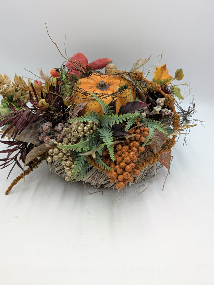 Herbstgesteck von der Seite: oranger Kürbis in Zweigkranz, orange und goldene Beeren, Farnwedel, dunkelrote Blätter