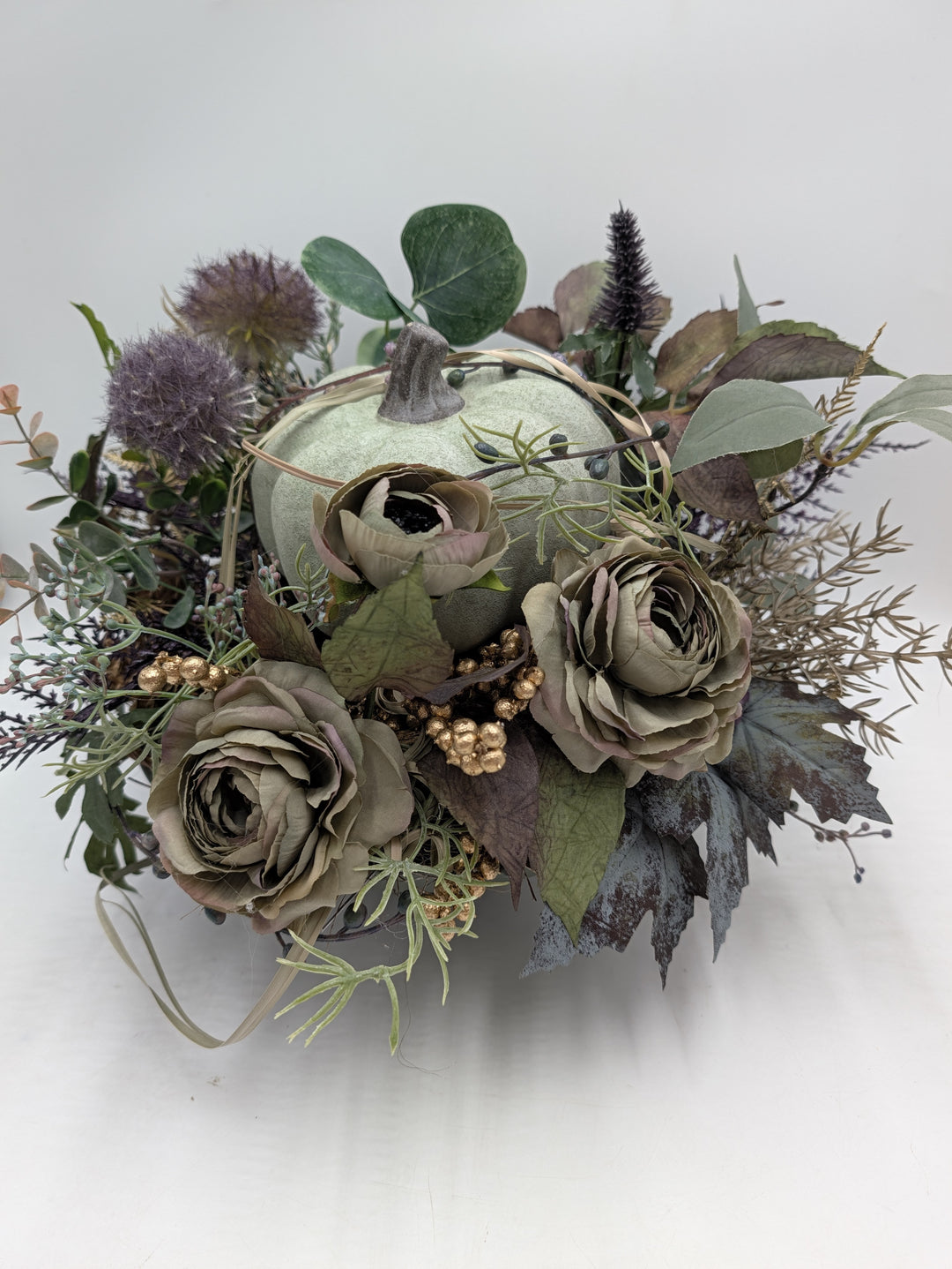 Herbstgesteck mit hellgrünem Kürbis, graugrünen Rosen, lila Disteln und goldenen Beeren