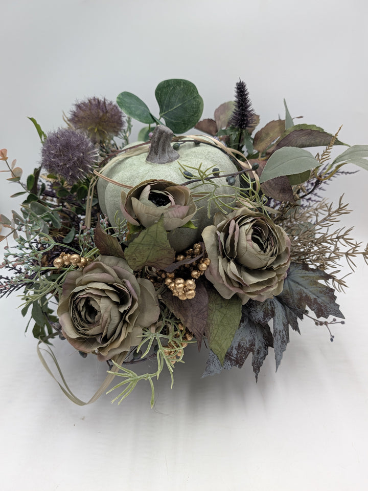 Herbstgesteck mit hellgrünem Kürbis, graugrünen Rosen, lila Disteln und goldenen Beeren