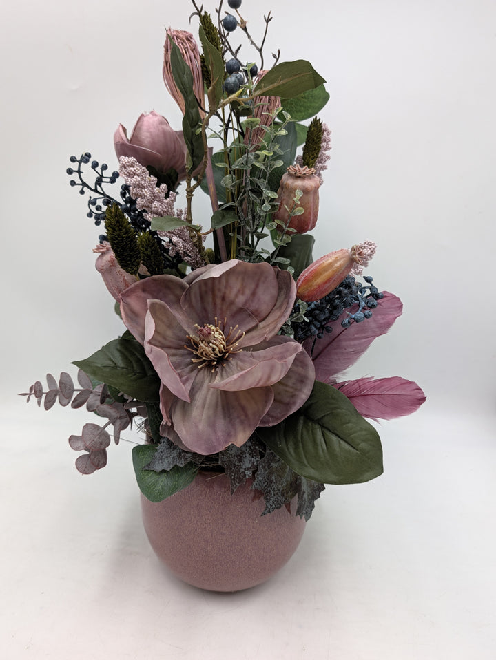 Gesteck mit altrosa Magnolie, blauen Beeren, Grasähren und Mohnkapseln in bauchiger rosa Keramikvase