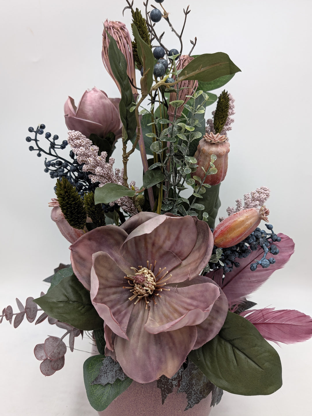 Nahaufnahme der geöffneten Magnolie mit hellen Staubgefäßen, daneben blaue Beeren, rosa Rispen und altrosa Federn