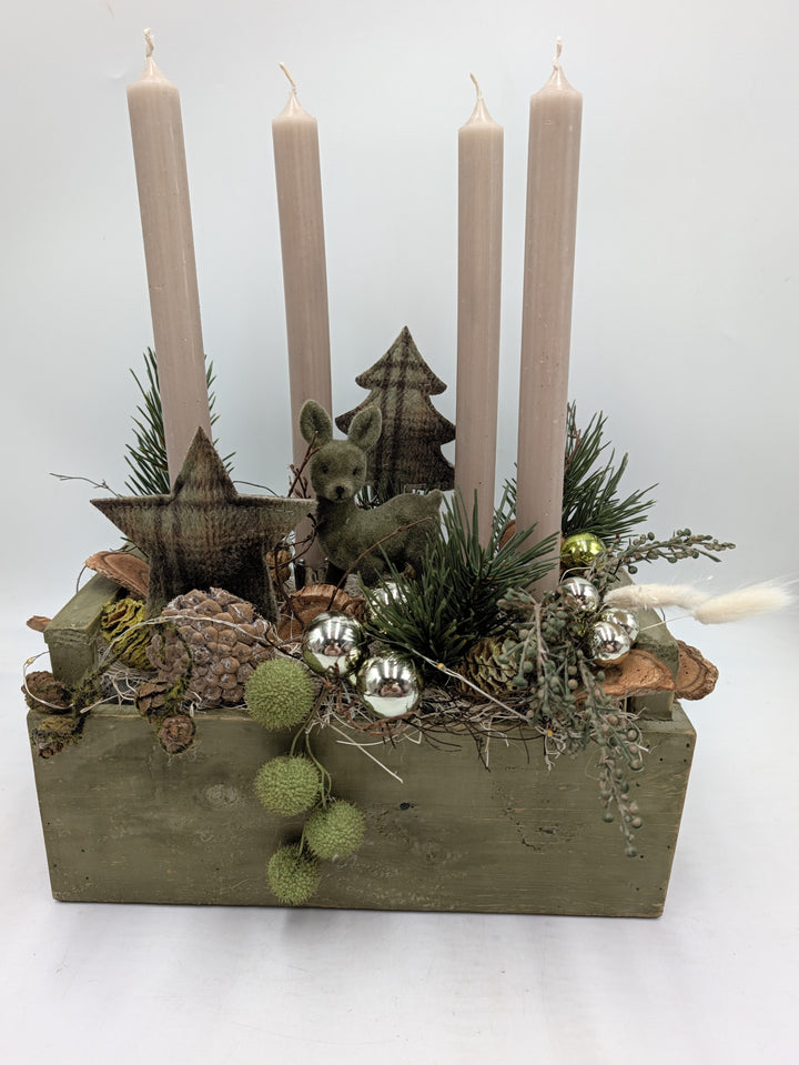 Adventsgesteck im grünen Holzkasten mit vier cremefarbenen Stabkerzen, Filzreh, Stern, Zapfen und Silberkugeln