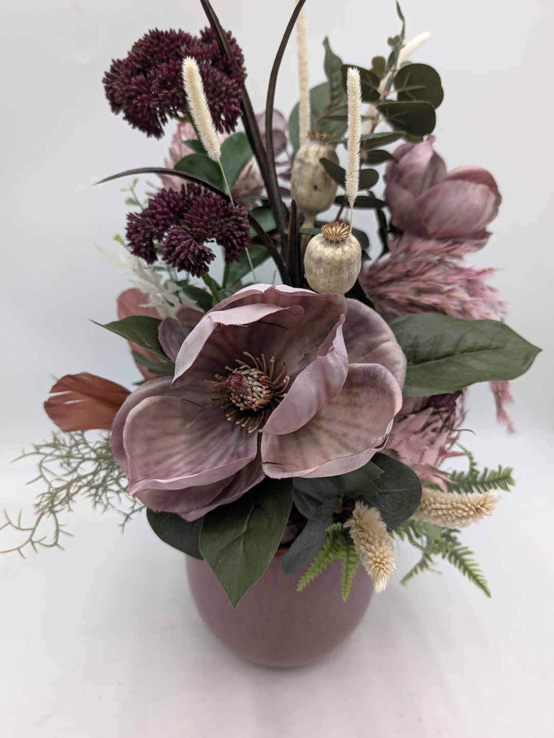 Nahaufnahme der altrosa Magnolienblüte mit Mohnkapseln, Proteen, Farn und cremefarbenen Gräsern