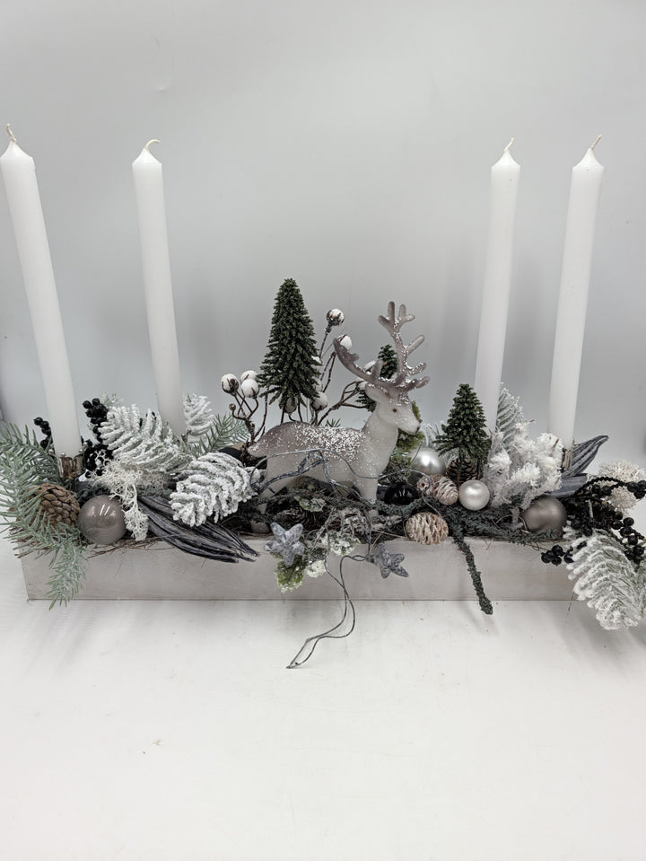 Längliches Adventsgesteck in Weiß und Grau mit Hirsch, Tannenbäumchen und vier weißen Stabkerzen im Holzkasten