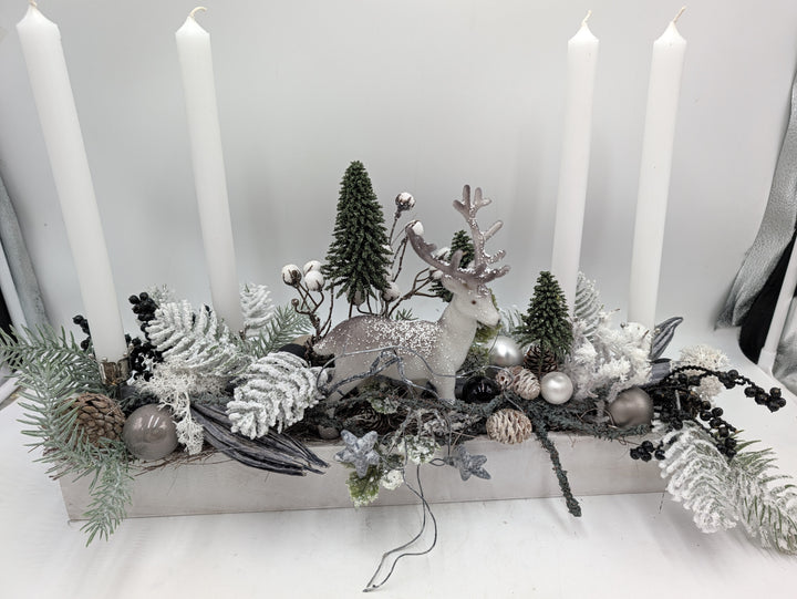 Nahansicht des Adventsgestecks mit weißem Hirsch, Zapfen, silbernen Kugeln, schwarzen Beeren und beschneiten Farnblättern