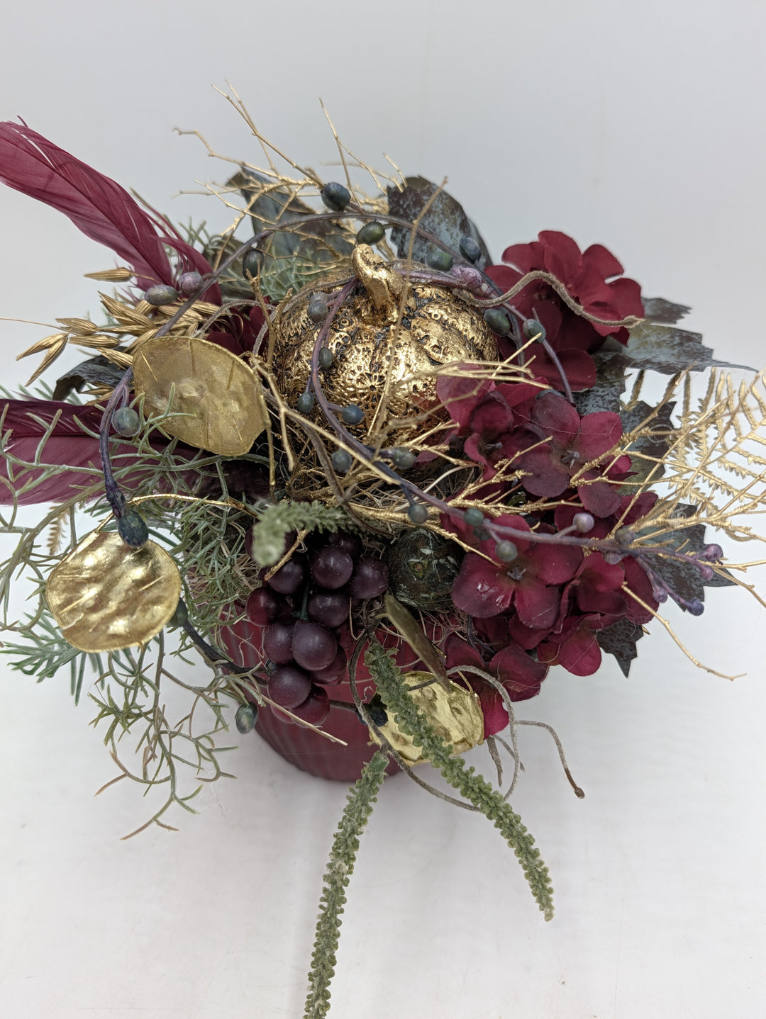 Gesteck von oben: goldener Kürbis zwischen Hortensien, goldenen Talern, Nadelzweigen und hängendem Amaranth