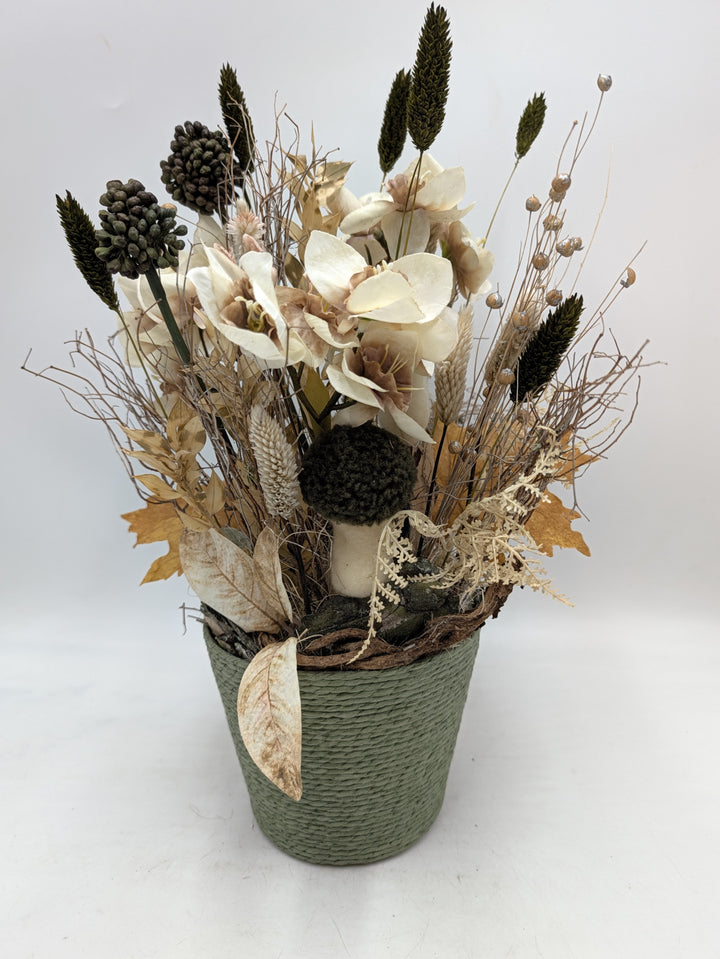 Herbstgesteck mit cremeweißen Amaryllisblüten, grünen Gräserähren und Pilz in grünem Kordeltopf