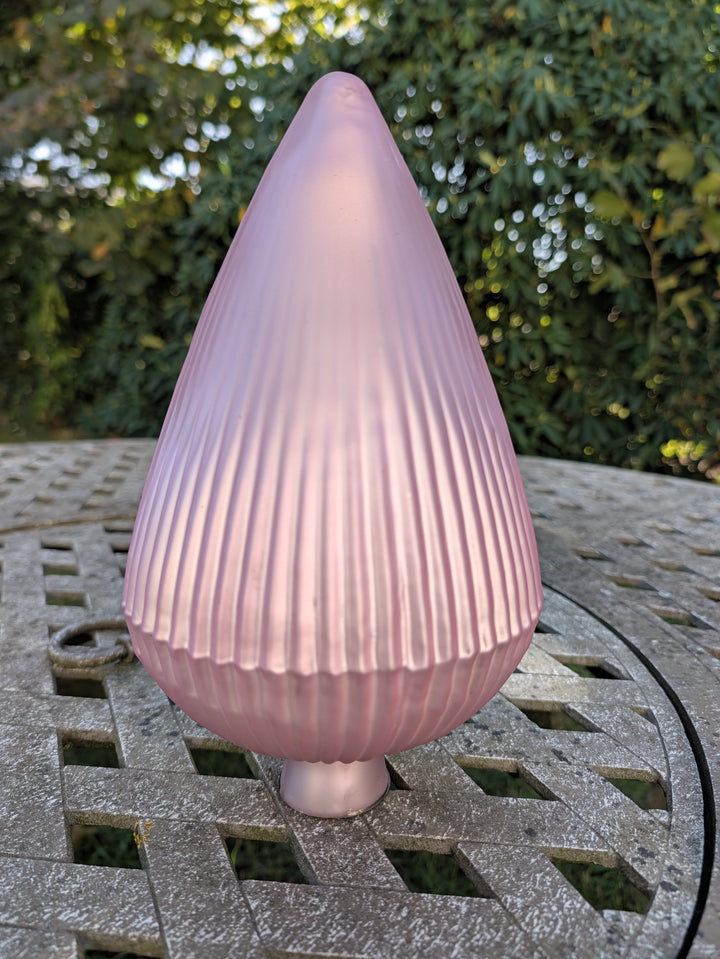 Geriffelte rosa Rosenkugel mit kurzem Steckzapfen auf grauem Gartentisch vor dunkelgrüner Hecke
