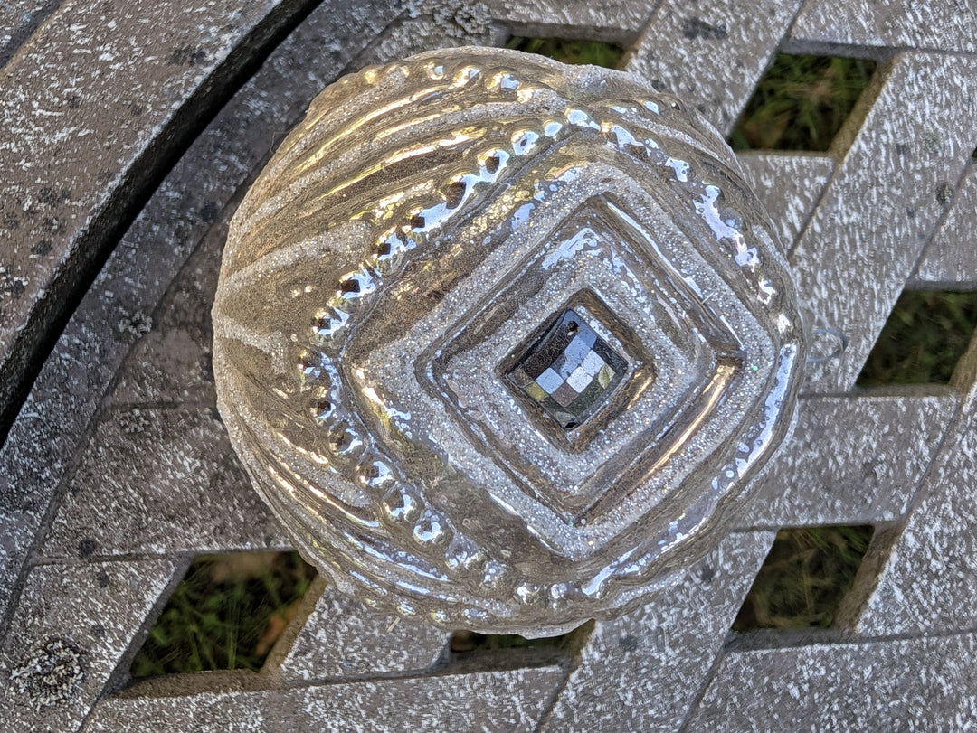 Silberne Christbaumkugel von oben mit Rautenrelief, facettiertem Stein in der Mitte und Perlenreihe