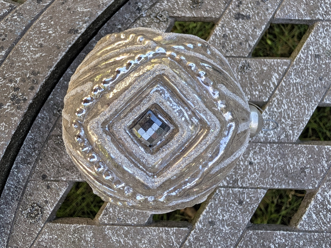 Silberne Christbaumkugel mit geriffeltem Relief und silberfarbener Aufhängekappe mit Öse