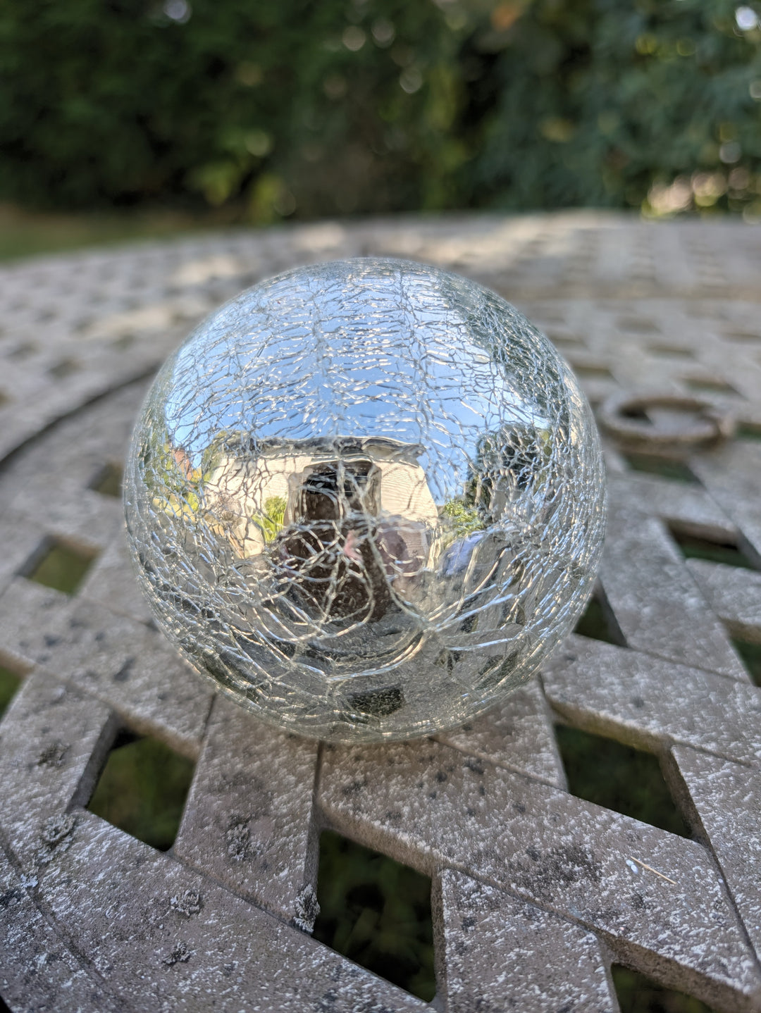 Verspiegelte Glaskugel in Silber mit feinen Rissen, liegend auf einem Gartentisch aus Metall