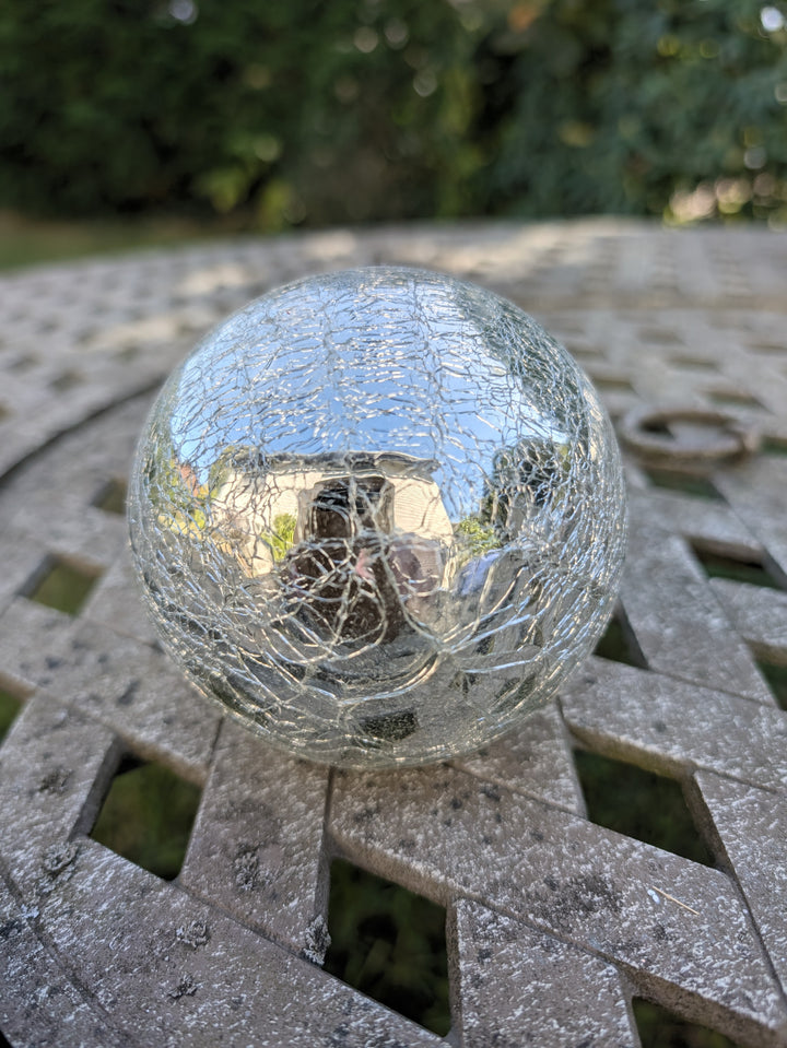 Verspiegelte Glaskugel in Silber mit feinen Rissen, liegend auf einem Gartentisch aus Metall