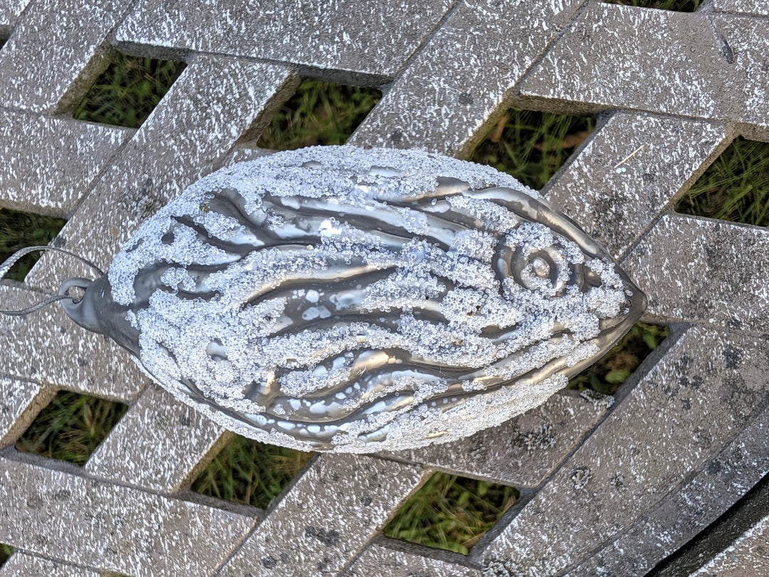 Grauer Baumschmuck in Tropfenform mit Aufhängeschlaufe, weiße Glitzerlinien auf glänzender Oberfläche
