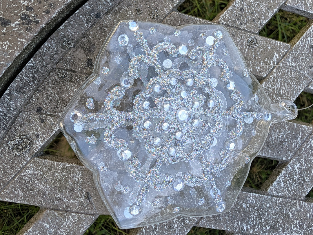 Glasstern mit sechs Zacken, Glitzerlinien und klaren Steinen, Aufhängefaden an der Öse, Nahaufnahme von oben