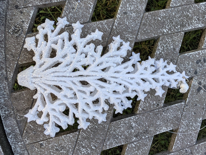 Weißer Schneeflocken-Anhänger mit Glitzer und feinen verzweigten Armen, liegend auf grauem Holzgitter