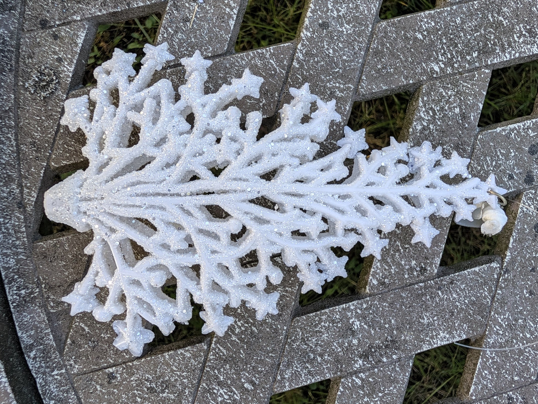 Schneeflocke aus weißem Baumschmuck mit Haken und durchsichtigem Faden am rechten Ende, Nahaufnahme