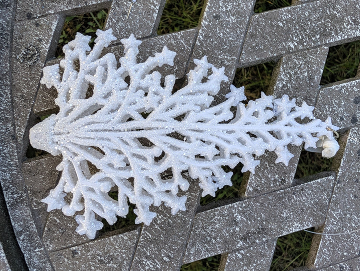 Schneeflocke aus weißem Baumschmuck mit Haken und durchsichtigem Faden am rechten Ende, Nahaufnahme