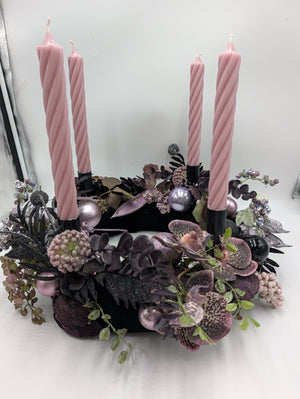 Adventskranz von der Seite: dunkle Eukalyptuszweige, schwarze Farnblätter, rosa Kugeln und vier Stabkerzen