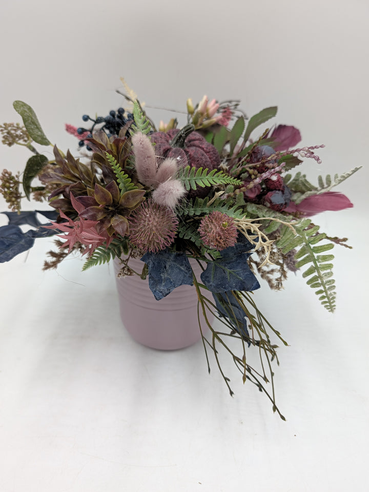 Herbstgesteck mit beerenrotem Kürbis, Farn, blauen Beeren und rosa Gräsern in altrosa Keramiktopf, seitlich