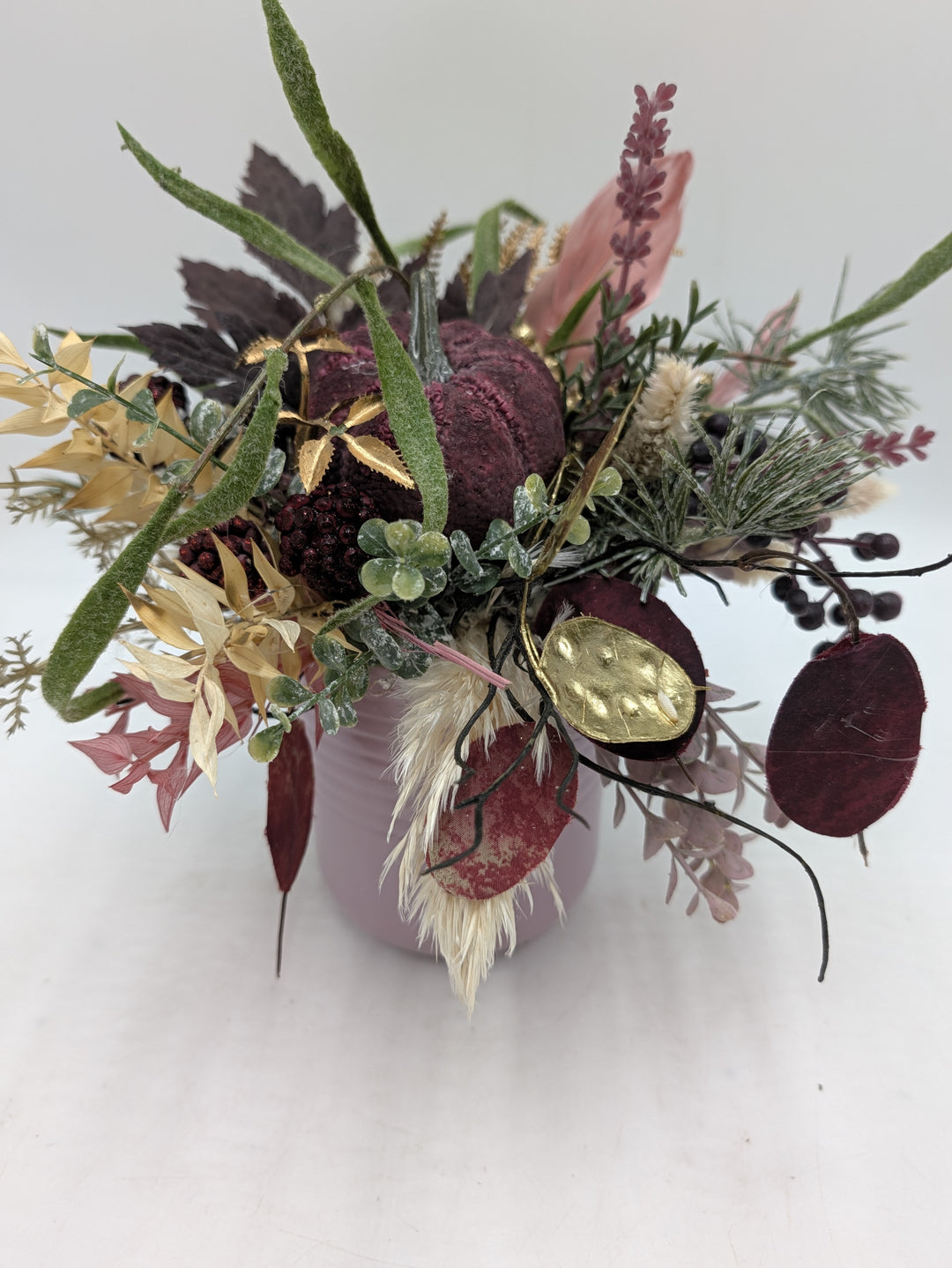 Herbstgesteck mit weinrotem Kürbis, goldenen Silberblatt-Scheiben und hellen Gräsern in rosa Keramikvase