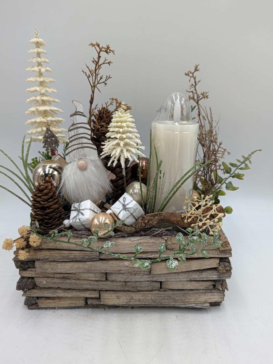 Weihnachtsgesteck mit Wichtel, cremefarbenen Bäumchen, Zapfen und weißer Kerze in eckigem Holzgefäß