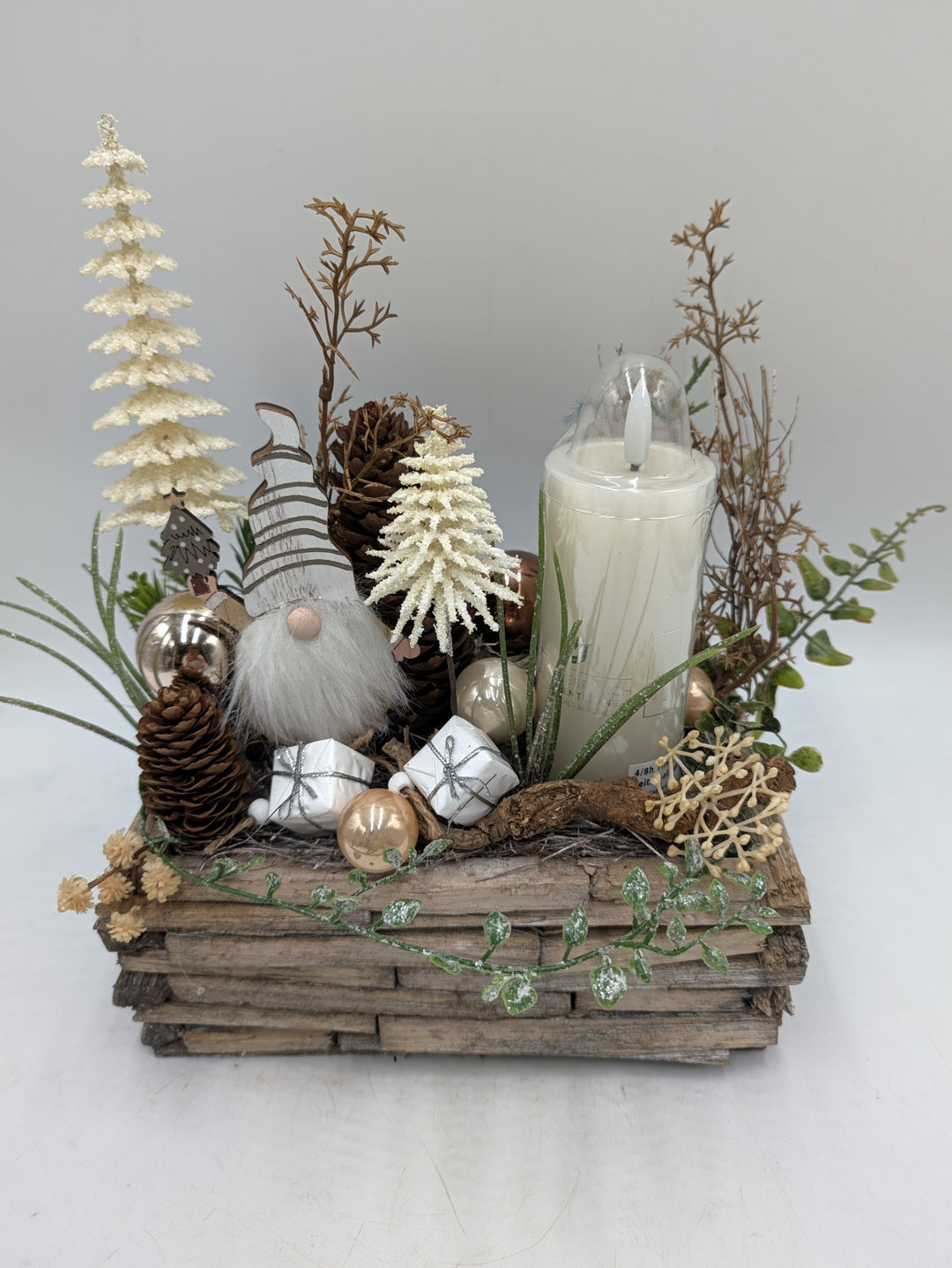 Weihnachtsgesteck in Creme und Natur mit Wichtel, Päckchen, Kugeln und LED-Kerze, seitlich fotografiert