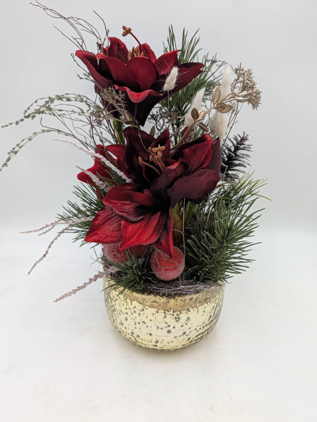 Weihnachtsgesteck seitlich: rote Amaryllis, Tanne, Zapfen, goldene Blätter und helle Gräser über gesprenkeltem Goldtopf