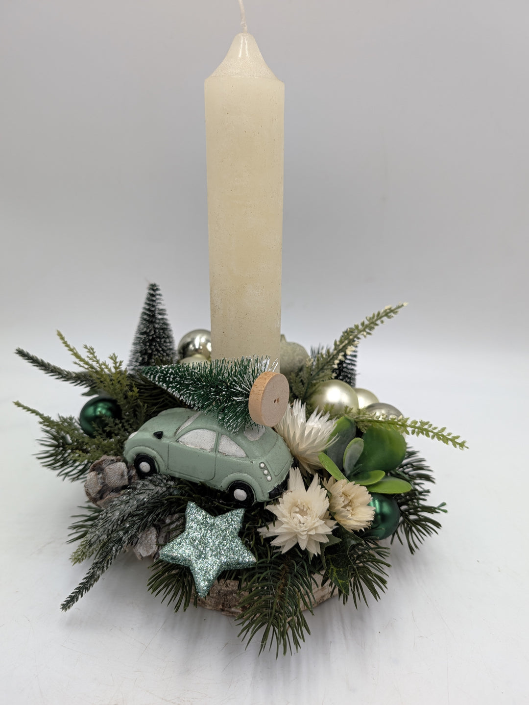 Weihnachtsgesteck mit cremefarbener Kerze, mintgrünem Auto mit Tannenbaum, Glitzerstern und Zapfen