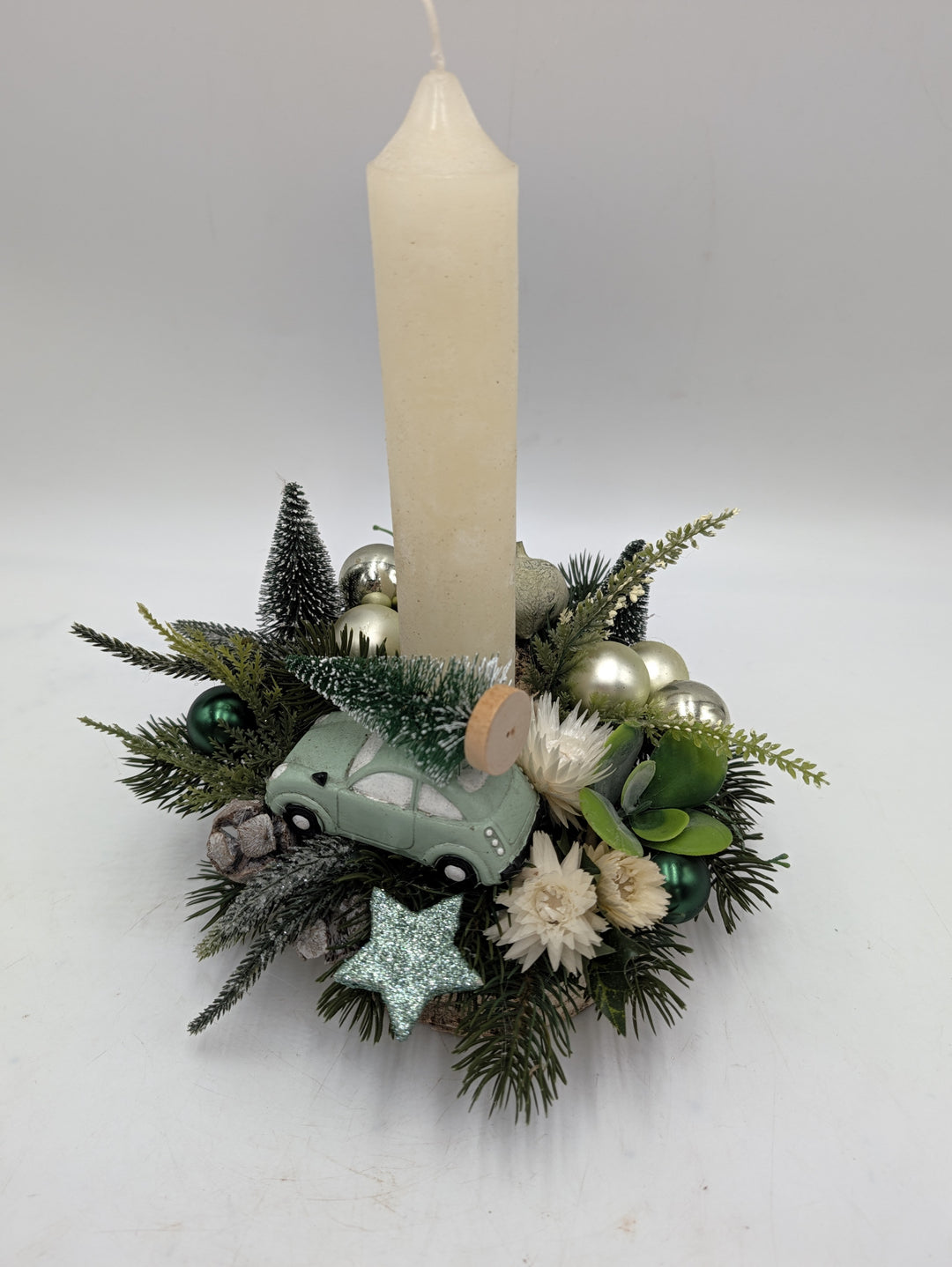Weihnachtsgesteck von der Seite mit Tannenzweigen, grünen Kugeln, Strohblumen und mintfarbenem Auto
