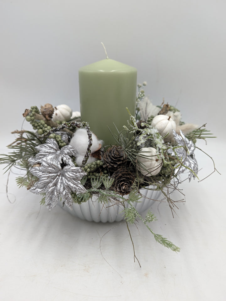 Wintergesteck mit mintgrüner Stumpenkerze, silbernen Blättern, Zapfen und Baumwolle in weißer geriffelter Schale