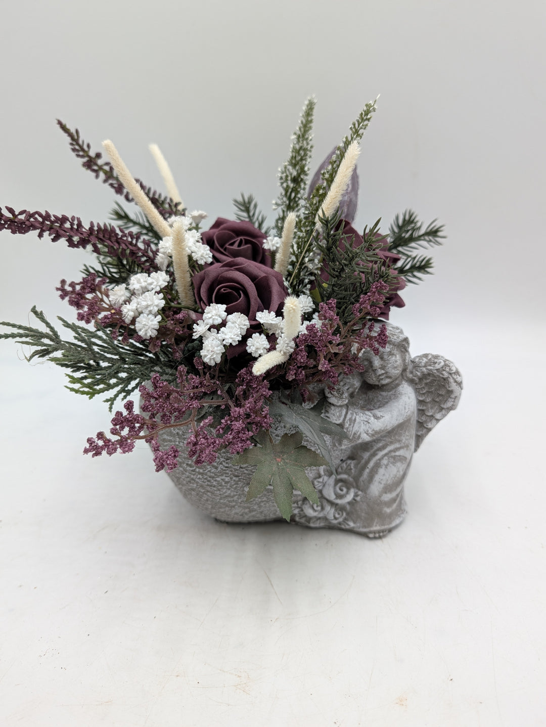Gesteck aus dunkellila Rosen, Heidekraut und cremefarbenen Gräsern im grauen Engel-Gefäß von vorn