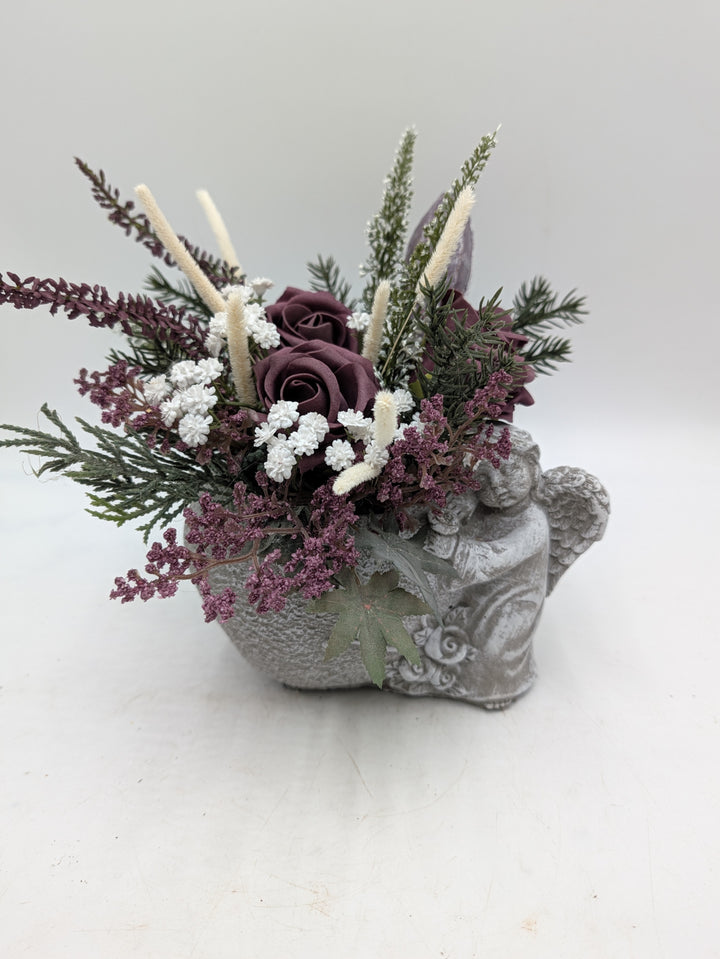 Gesteck aus dunkellila Rosen, Heidekraut und cremefarbenen Gräsern im grauen Engel-Gefäß von vorn