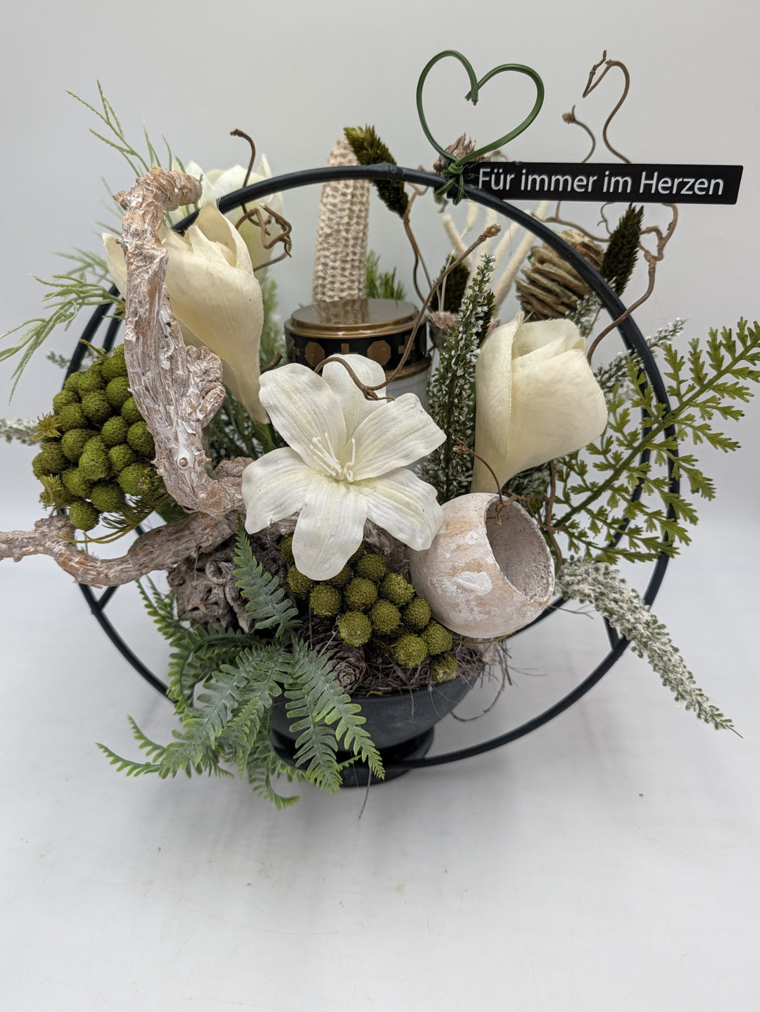 Grabgesteck in schwarzer Schale mit weißer Amaryllis, grünen Kugeln, Farn und Grablicht im schwarzen Metallring