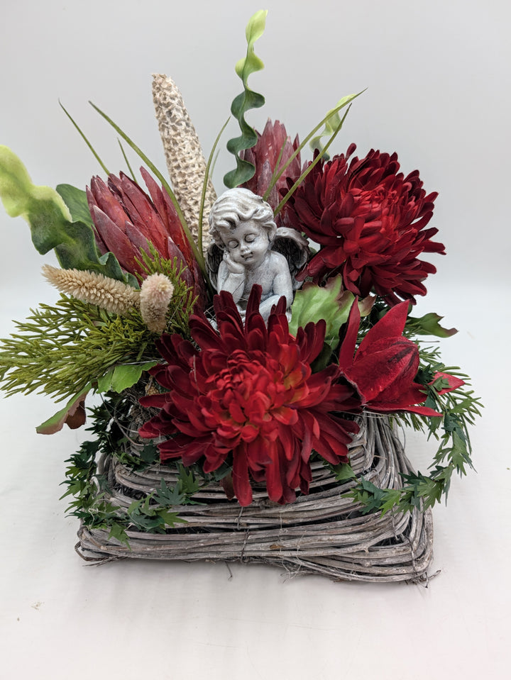 Trauergesteck in eckigem grauem Korb mit roten Chrysanthemen, Protea, Gräsern und weißer Engelsfigur