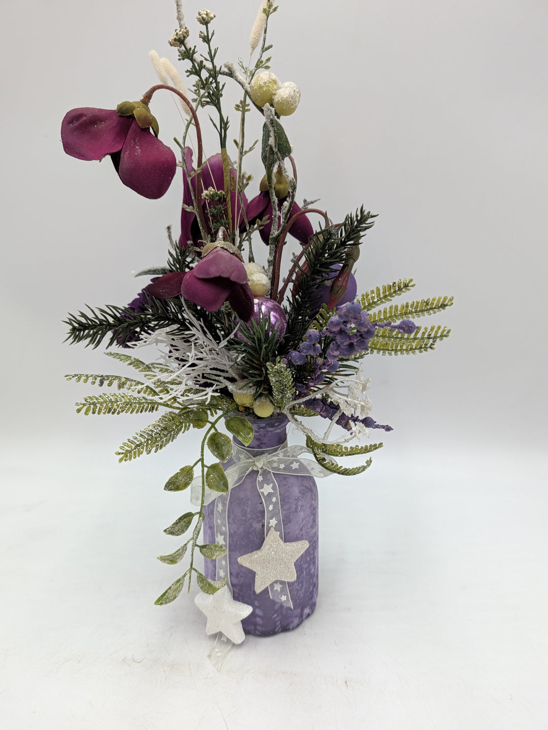 Wintergesteck in lilafarbener Vase mit Sternen, Alpenveilchen, Tannenzweigen, Farn und weißen Gräsern
