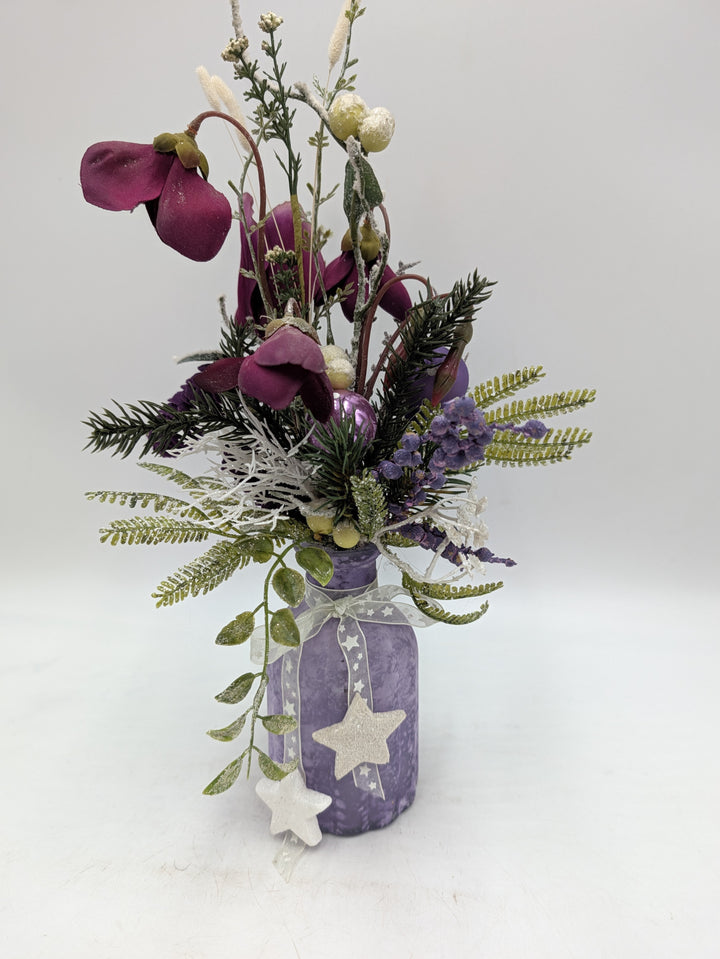 Wintergesteck in lilafarbener Vase mit Sternen, Alpenveilchen, Tannenzweigen, Farn und weißen Gräsern