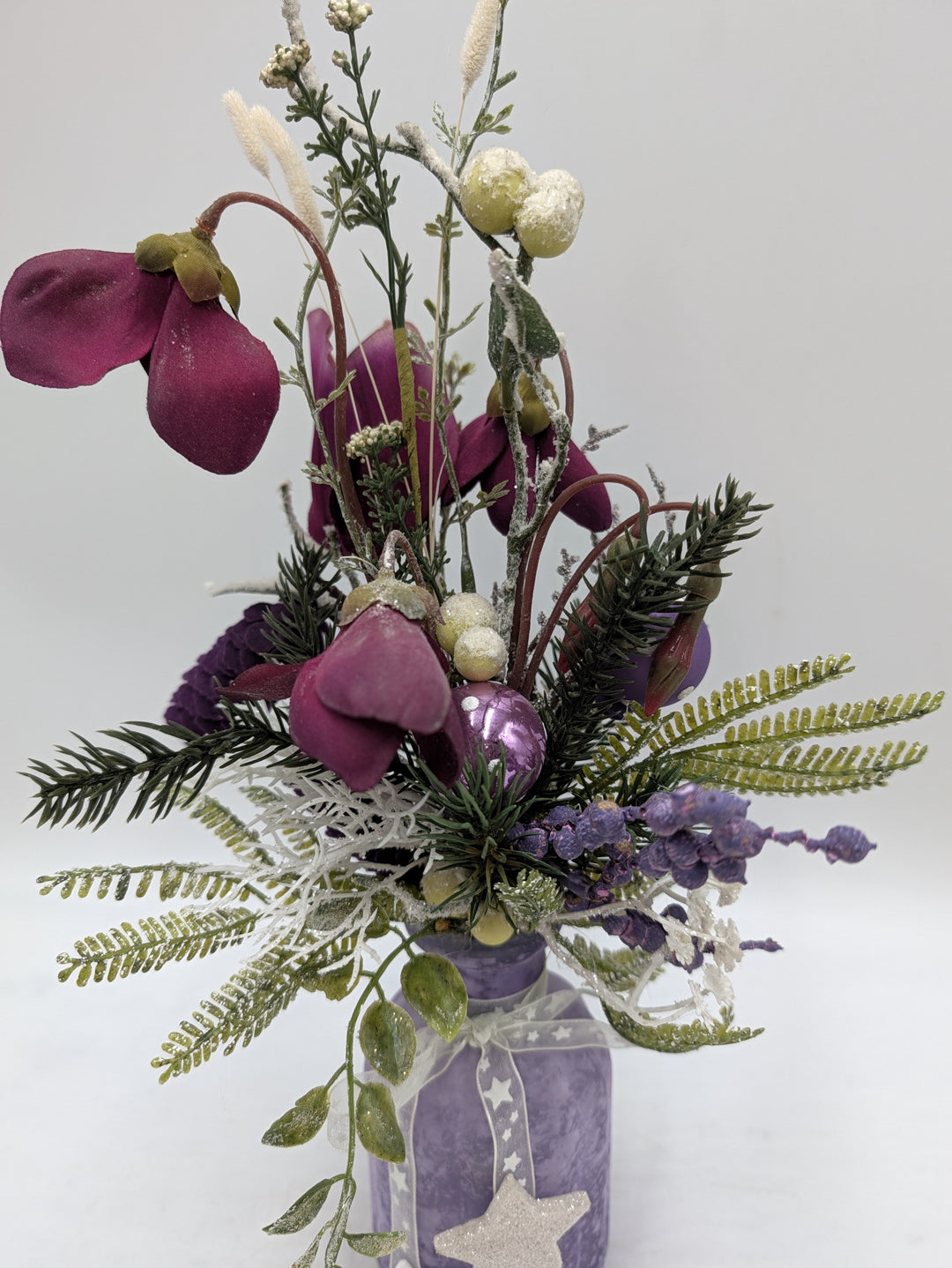Nahaufnahme des Gestecks: lila Alpenveilchenblüten, cremefarbene Beeren, lila Kugel und grüne Farnwedel