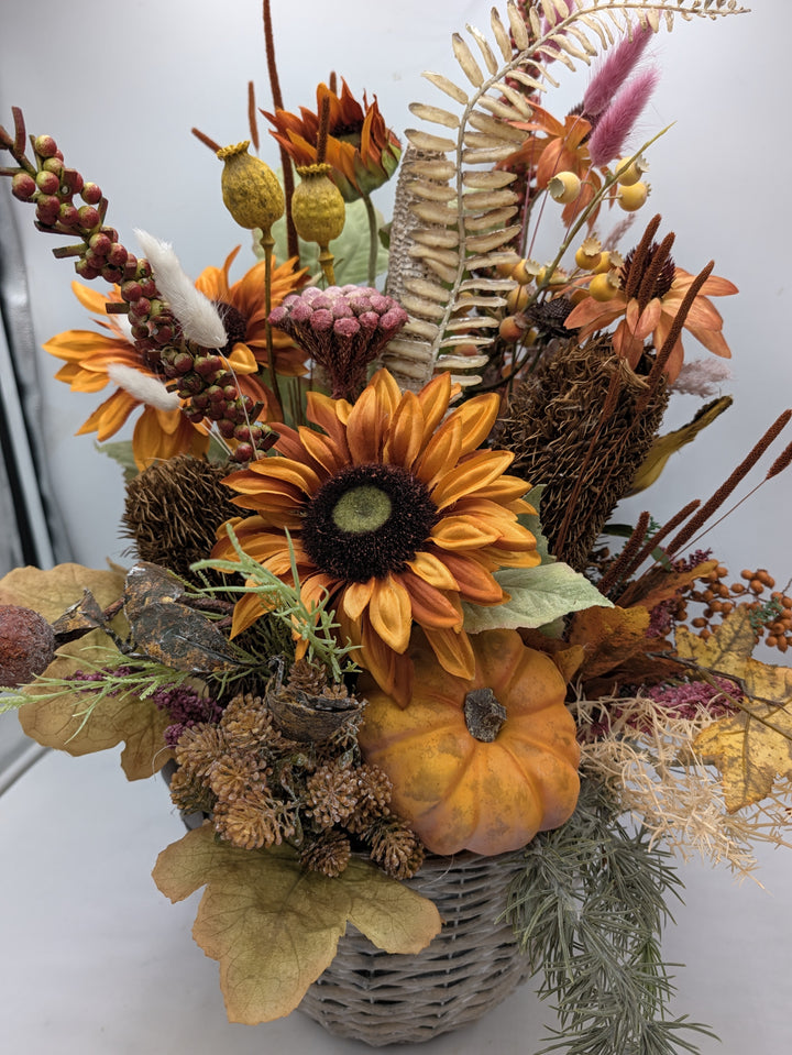 Herbstgesteck von vorn: Sonnenblume mit braunem Herz, kleiner Kürbis, Mohnkapseln, Beeren und Herbstlaub