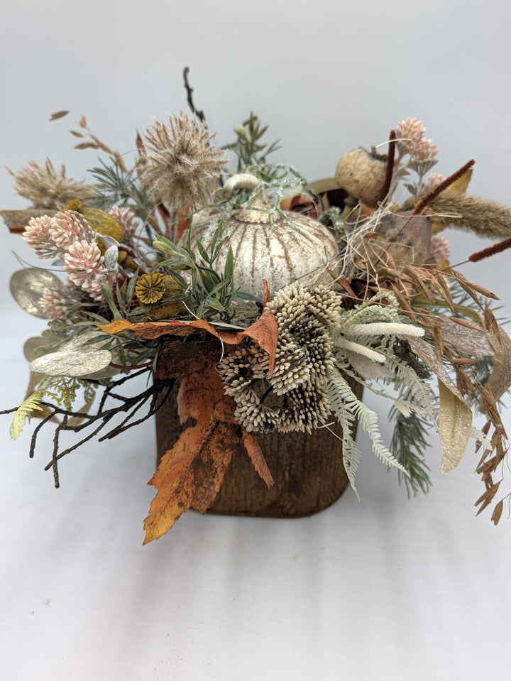 Herbstgesteck mit hellem Kürbis, Disteln, Gräsern und orangefarbenem Laub in eckigem braunem Gefäß
