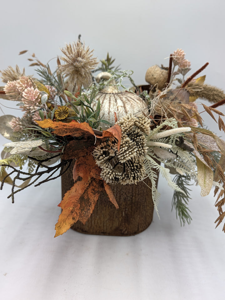 Herbstgesteck von vorn: cremefarbene Blütenbällchen, rosa Blüten, Farn und Gräser rund um einen Kürbis