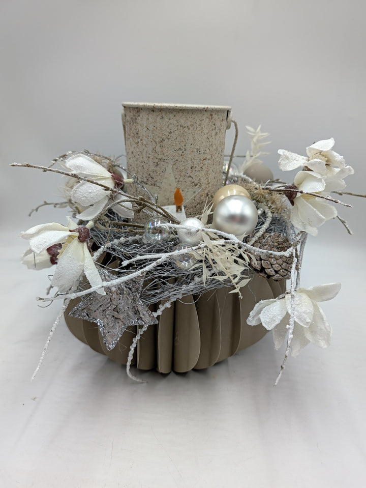 Wintergesteck in Taupe-Gefäß mit hellem Windlicht, weißen Magnolien, silbernen Kugeln und Rindenstern