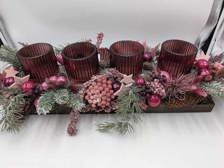 Adventsgesteck von vorne: rosa Beerenkugel, Holzsterne, Zapfen und dunkellila Trauben zwischen geriffelten Gläsern
