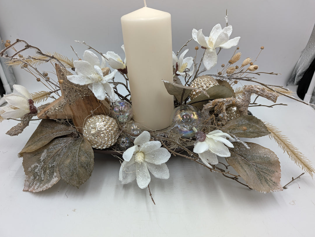 Wintergesteck mit cremefarbener Stumpenkerze, weißen Magnolien, Holzstern und Kugeln in Champagner