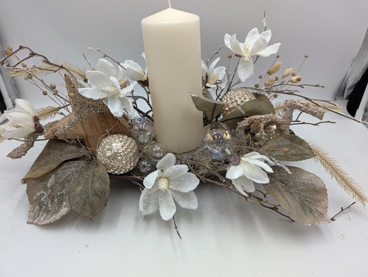 Wintergesteck mit cremefarbener Stumpenkerze, weißen Magnolien, Holzstern und Kugeln in Champagner