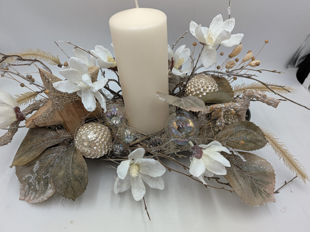 Längliches Wintergesteck von vorn: Kerze, glitzernde Magnolienblüten, olivfarbene Blätter und Glaskugeln