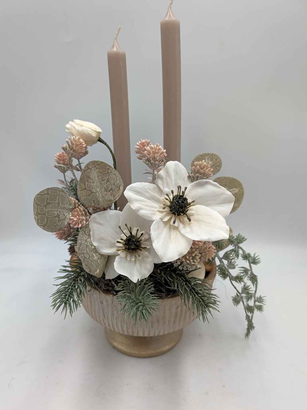 Wintergesteck mit zwei rosé Stabkerzen, cremeweißen Blüten, goldbeigen Blättern und Tanne in geriffelter Schale